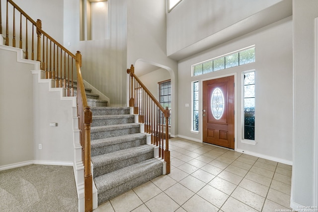 entryway featuring a towering ceiling, stairway, baseboards, and light tile patterned flooring