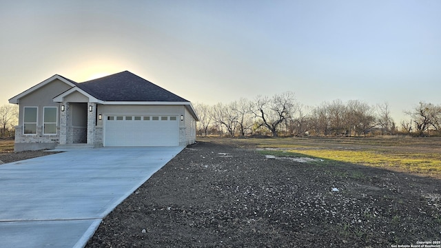 exterior space featuring stone siding, driveway, an attached garage, and stucco siding