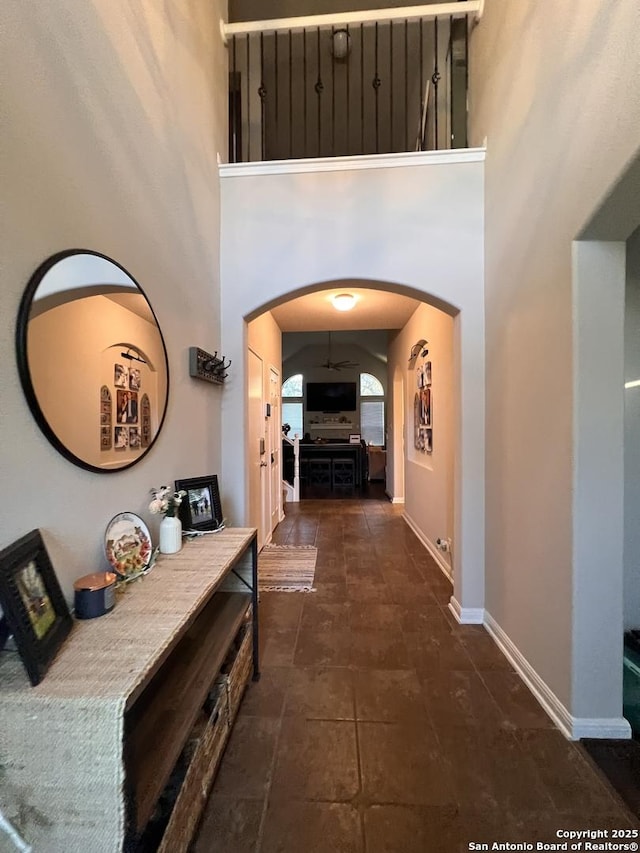 corridor with a towering ceiling, baseboards, and arched walkways