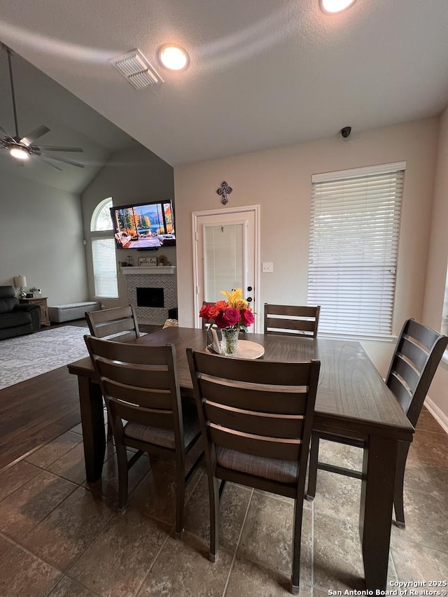 dining room featuring visible vents, vaulted ceiling, a textured ceiling, ceiling fan, and a tile fireplace