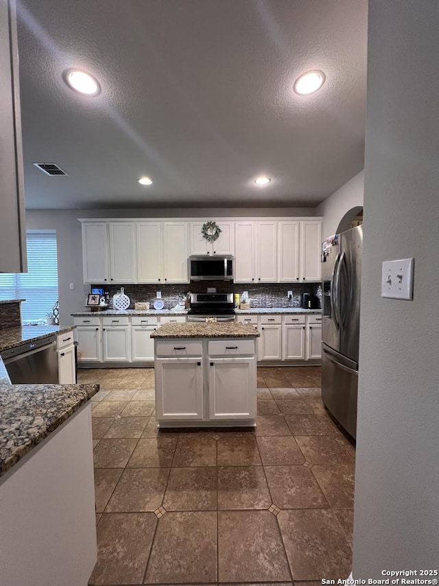 kitchen featuring white cabinets, tasteful backsplash, dark stone counters, and stainless steel appliances