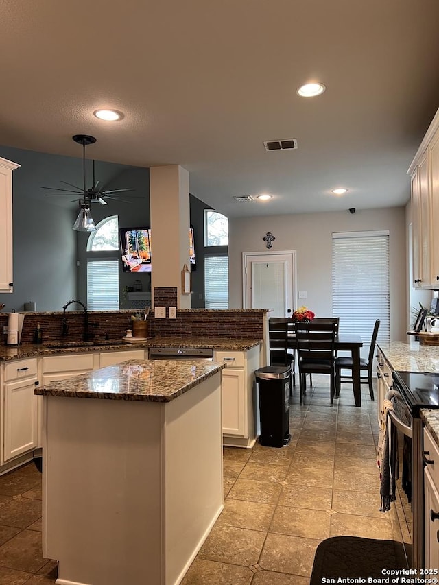 kitchen with a sink, visible vents, white cabinets, a center island, and dark stone counters