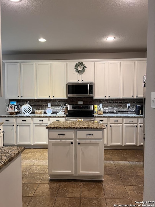 kitchen with appliances with stainless steel finishes, white cabinetry, and dark stone countertops