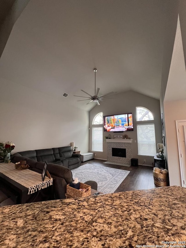 living area with dark wood-style flooring, a fireplace, lofted ceiling, visible vents, and ceiling fan