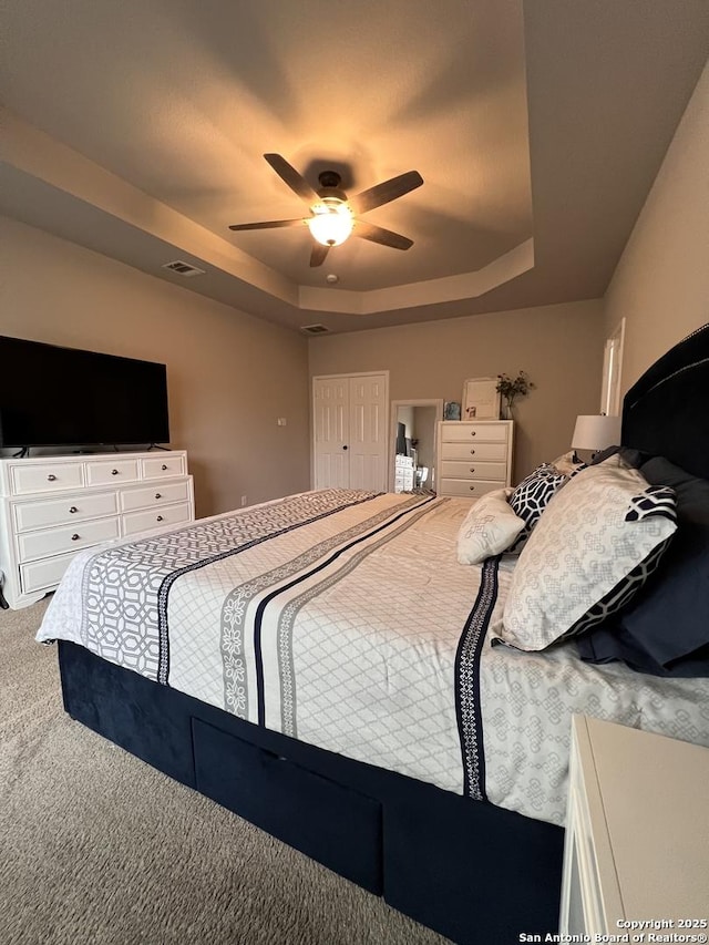 carpeted bedroom with visible vents, a tray ceiling, and ceiling fan