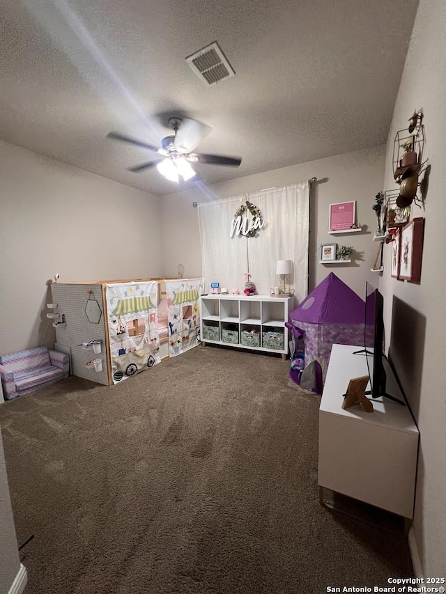 playroom featuring carpet, visible vents, ceiling fan, and a textured ceiling