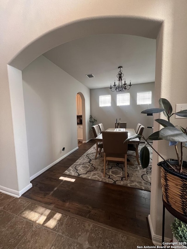 dining room with arched walkways, dark wood-type flooring, visible vents, and baseboards