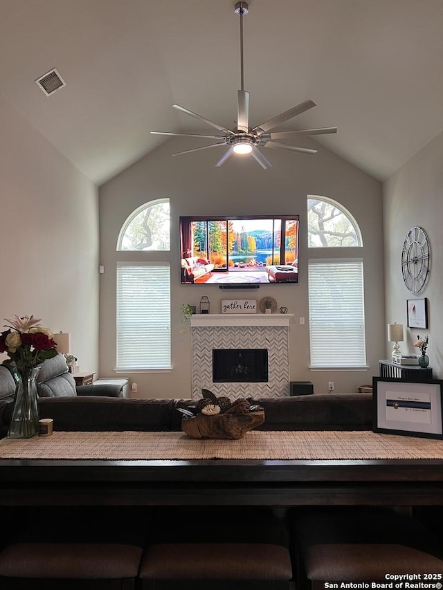 living area with a wealth of natural light, a tile fireplace, visible vents, and vaulted ceiling