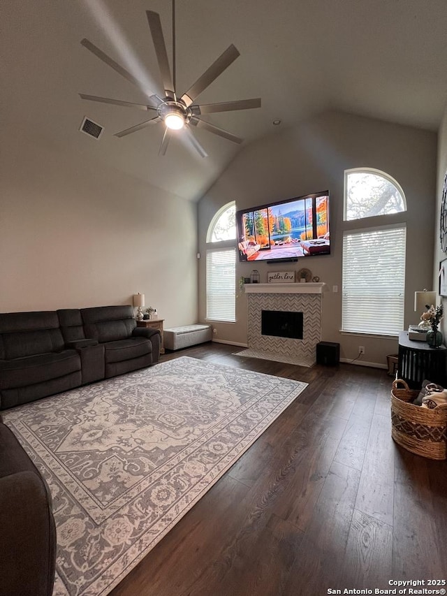 living area with ceiling fan, visible vents, vaulted ceiling, a tiled fireplace, and dark wood finished floors