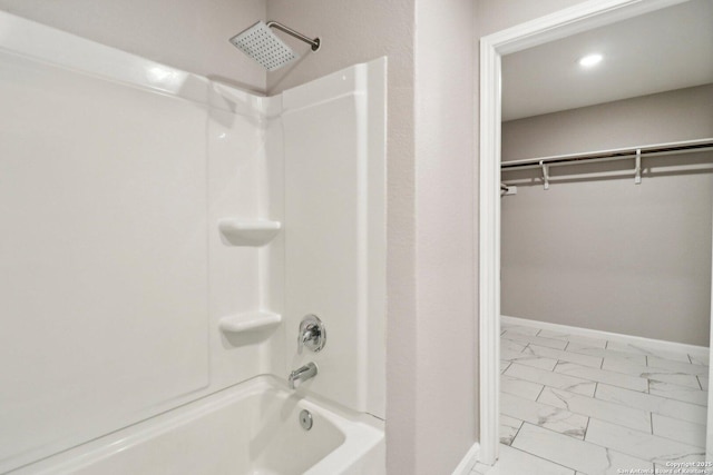 full bathroom with marble finish floor, a walk in closet, washtub / shower combination, and baseboards