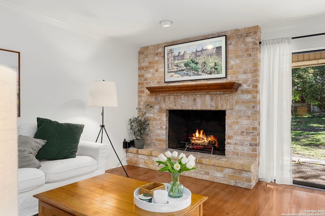 living area with a brick fireplace, ornamental molding, and wood finished floors