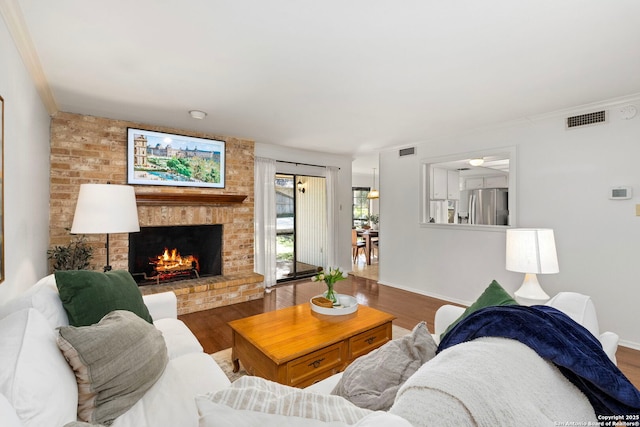 living room with a brick fireplace, visible vents, baseboards, and wood finished floors