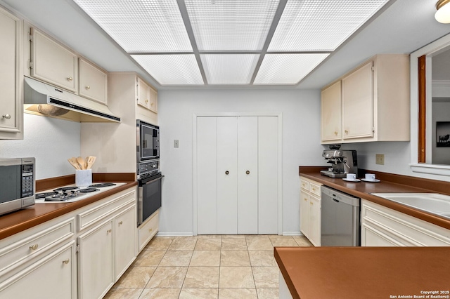 kitchen featuring light tile patterned flooring, under cabinet range hood, cream cabinetry, black appliances, and dark countertops