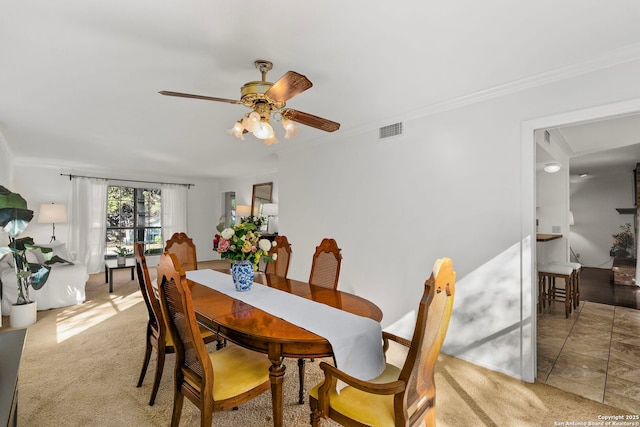 dining area featuring ornamental molding, a ceiling fan, visible vents, and light colored carpet