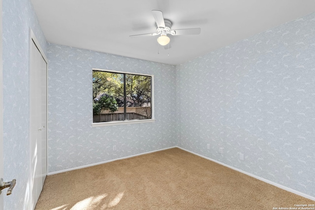 empty room with carpet floors, a ceiling fan, baseboards, and wallpapered walls