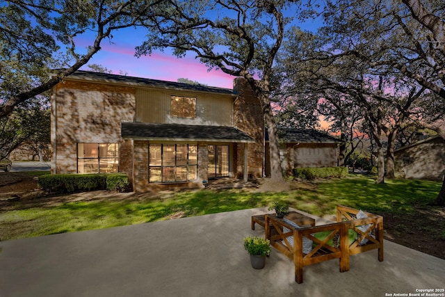 back of property at dusk featuring a chimney, a lawn, and a patio area