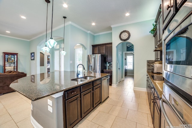 kitchen with a sink, appliances with stainless steel finishes, dark stone counters, an island with sink, and decorative light fixtures