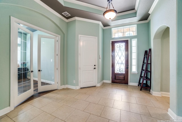 foyer entrance with crown molding, light tile patterned floors, a raised ceiling, visible vents, and baseboards