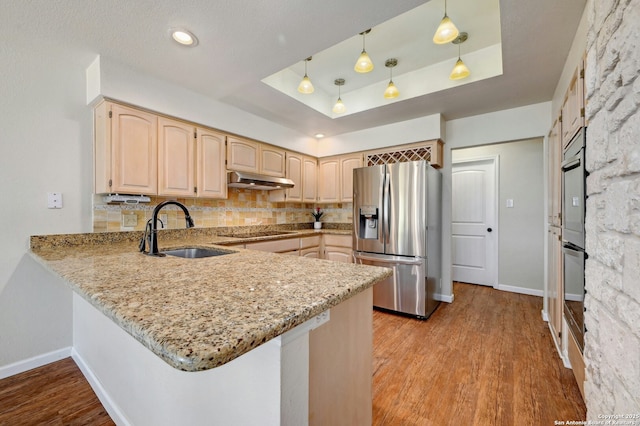 kitchen with stainless steel refrigerator with ice dispenser, a raised ceiling, a sink, under cabinet range hood, and black electric cooktop