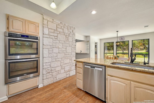 kitchen featuring light wood finished floors, light brown cabinetry, appliances with stainless steel finishes, a sink, and light stone countertops