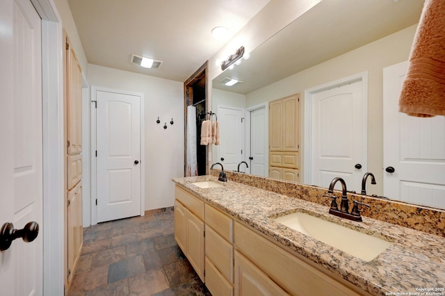 full bathroom with double vanity, stone finish floor, a sink, and visible vents