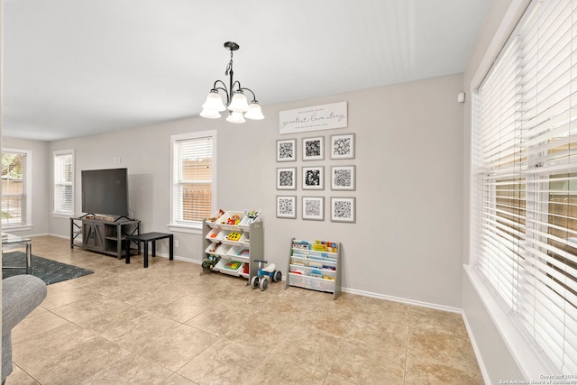 rec room with a chandelier, baseboards, light tile patterned flooring, and a healthy amount of sunlight