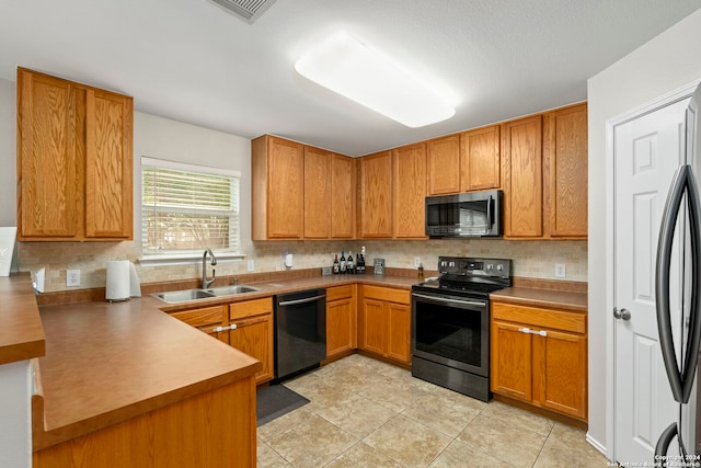 kitchen with tasteful backsplash, appliances with stainless steel finishes, brown cabinets, a sink, and light tile patterned flooring