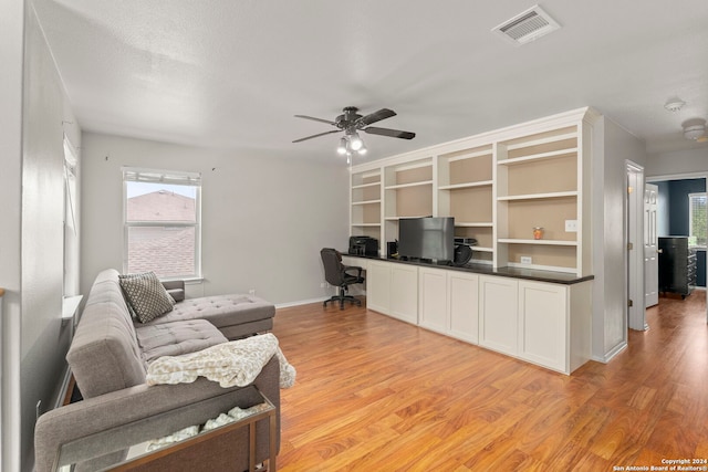 office area with light wood finished floors, baseboards, visible vents, ceiling fan, and built in desk