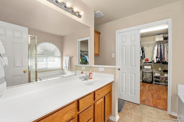 bathroom with visible vents, tile patterned floors, a garden tub, a walk in closet, and vanity