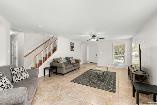 living room featuring arched walkways, light tile patterned floors, stairway, ceiling fan, and baseboards