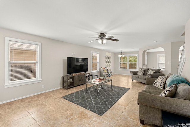 living area featuring ceiling fan with notable chandelier, arched walkways, baseboards, and light tile patterned floors