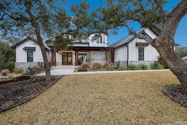 modern inspired farmhouse with metal roof, stone siding, french doors, a front lawn, and board and batten siding