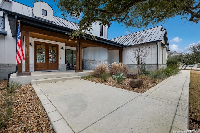 exterior space with french doors, covered porch, a standing seam roof, metal roof, and stone siding