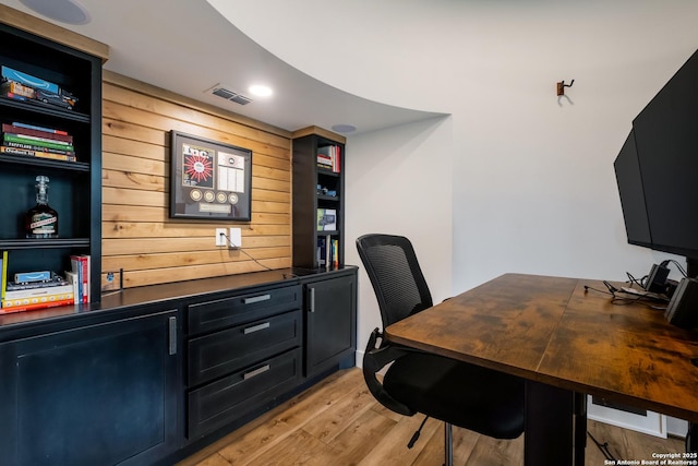 office with light wood-style flooring, wood walls, and visible vents