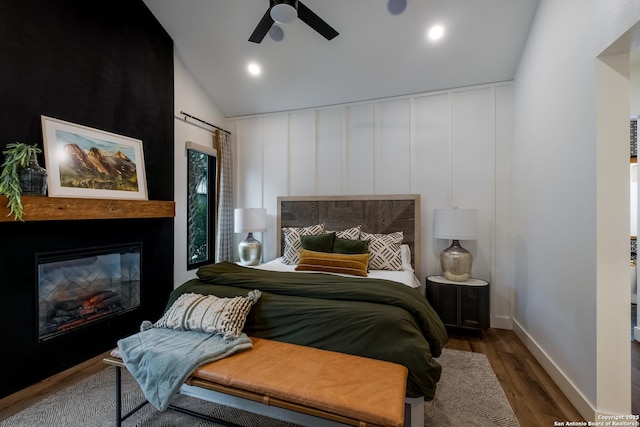 bedroom featuring a ceiling fan, a glass covered fireplace, wood finished floors, vaulted ceiling, and recessed lighting