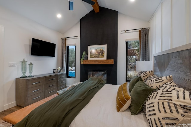 bedroom featuring vaulted ceiling with beams, ceiling fan, a barn door, a large fireplace, and light wood-type flooring