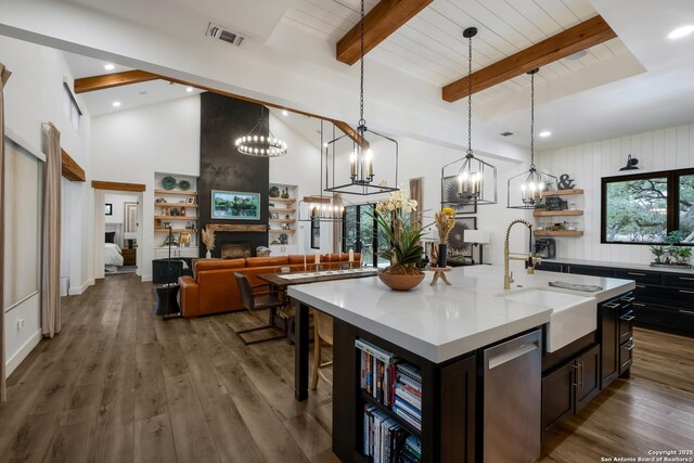 kitchen featuring light countertops, stainless steel dishwasher, beam ceiling, an island with sink, and pendant lighting