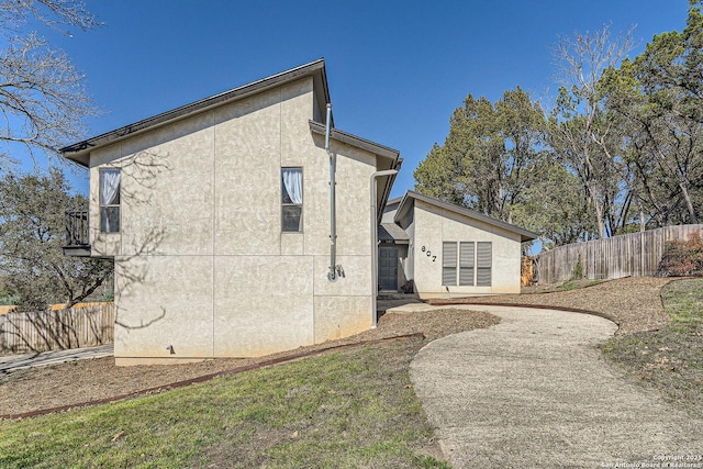 view of property exterior with fence, a balcony, and stucco siding