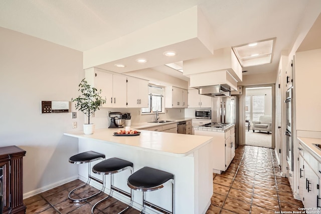 kitchen with light countertops, appliances with stainless steel finishes, white cabinetry, a sink, and a peninsula