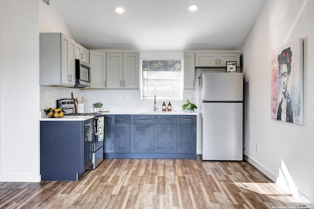 kitchen with a sink, light wood-style floors, light countertops, appliances with stainless steel finishes, and decorative backsplash