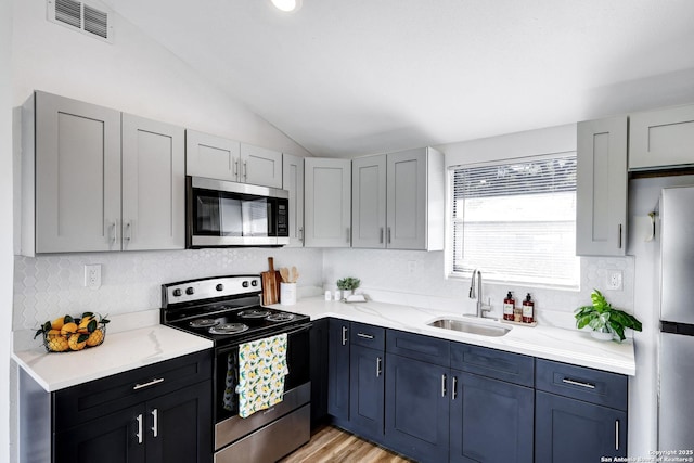 kitchen featuring lofted ceiling, visible vents, backsplash, appliances with stainless steel finishes, and a sink