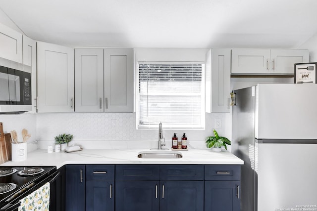 kitchen with blue cabinets, freestanding refrigerator, stainless steel microwave, and a sink