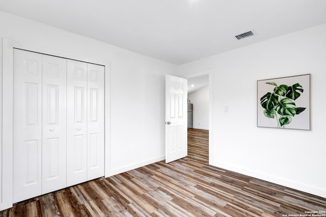 unfurnished bedroom with a closet, visible vents, baseboards, and wood finished floors