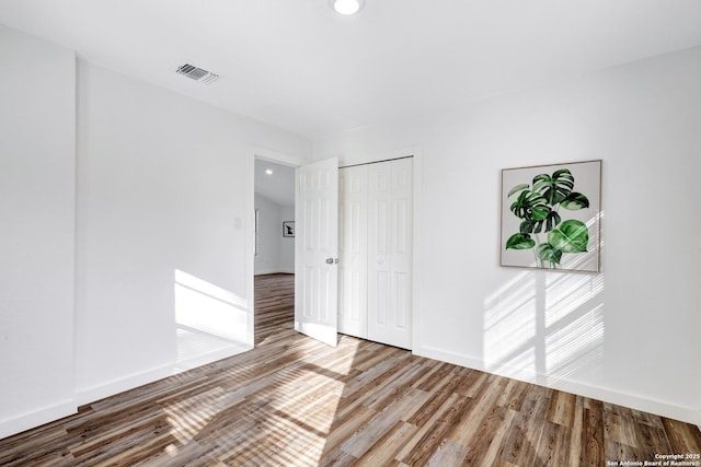 empty room featuring wood finished floors, visible vents, and baseboards