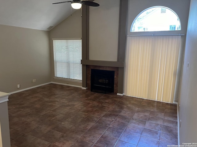 unfurnished living room with high vaulted ceiling, a tiled fireplace, a ceiling fan, and baseboards