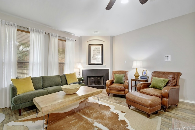 sitting room with baseboards, a tiled fireplace, a ceiling fan, and light wood-style floors