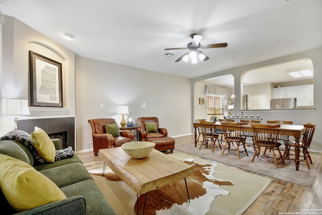 living room featuring light wood finished floors, visible vents, baseboards, ceiling fan, and a fireplace