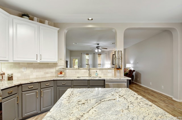 kitchen featuring light stone counters, a sink, white cabinetry, stainless steel dishwasher, and gray cabinets