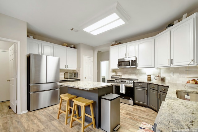 kitchen featuring white cabinetry, a kitchen island, appliances with stainless steel finishes, and light stone counters