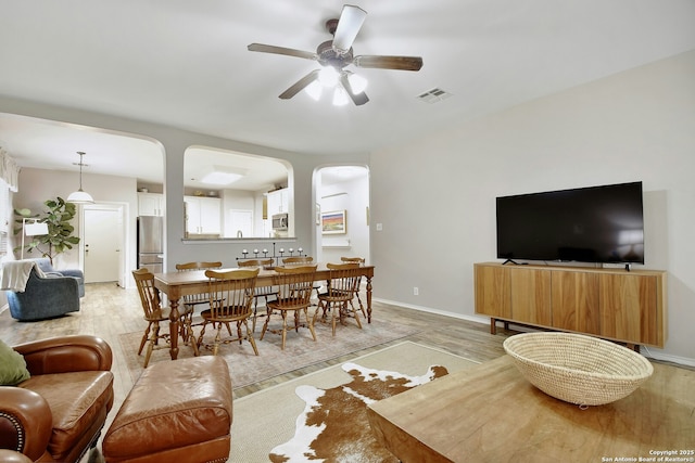 living area with arched walkways, light wood-type flooring, visible vents, and a ceiling fan